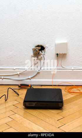 Fiber optic installation on home wall with obsolete CATV and new FTTH fiber outlets and internet receiver on parquet floor Stock Photo