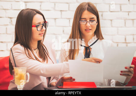 Successful teamwork: two young  business women sitting at desk talking about reports and finance. - Imag Stock Photo
