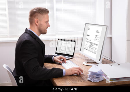 Happy Young Businessman Looking At Invoice On Computer Screen Near Laptop Stock Photo