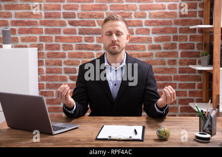 Relaxed Young Businessman Doing Meditation In Office Stock Photo
