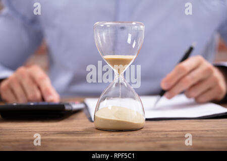Close-up Of A Hourglass In Front Of Businessman Working In Office Stock Photo