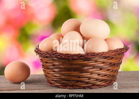 eggs on a wooden table in a wicker basket with blurred garden background Stock Photo