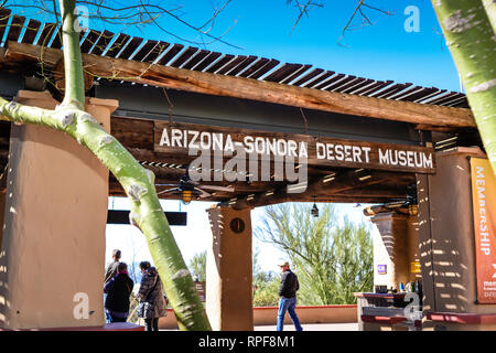 Visitors strolling under the rustic hand carved wooden sign hanging above the entrance to the Arizona-Sonora Desert Museum in Tucson, AZ Stock Photo
