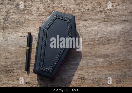 Leather book with cover in shape of Coffin. The book is captured closed and frontal while standing on the wooden table Stock Photo