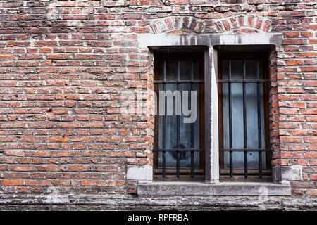 Old wooden windows with metal bars on the old brick house. Old house with copy space on the red bricks wall Stock Photo