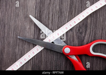 Red tailors scissors cutting the meter. Tailor concept with copy space above wooden background Stock Photo