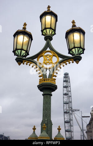 Ornate triple headed cast iron  lamp post with lights lit on Westminster Bridge  England London with the London eye in the background Stock Photo