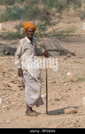 Native man standing with cane in desert, Jaisalmer, Rajasthan, India