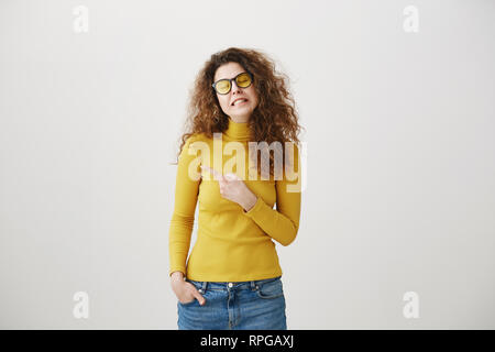 Excited young woman pointing her finger towards blank space isolated over grey background. Stock Photo