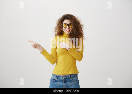 Excited young woman pointing her finger towards blank space isolated over grey background. Stock Photo