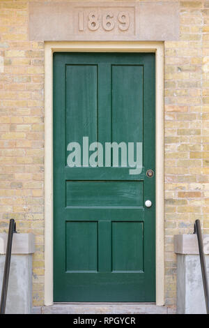 Green door in a yellow brick building that dates to 1869 as indicated by the stone header.  Entry to the historic Cana Island Lighthouse in Door Count Stock Photo