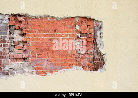 Stucco exterior wall with exposed or damaged area revealing weathered old brick pattern, suitable for a background with copy space or copyspace. Stock Photo