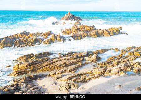Storm waves crashing into rhyolite rocky foreshore at base of Mount Maunganui looking out to North Rock beacon. Stock Photo