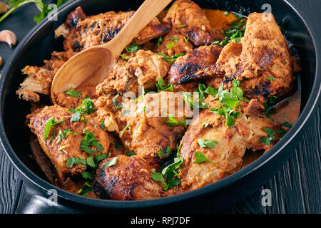 Kuku Paka, Kenyan chargrilled Chicken stewed in creamy spicy Coconut Sauce in a earthenware dutch oven on a wooden table, view from above, close-up Stock Photo