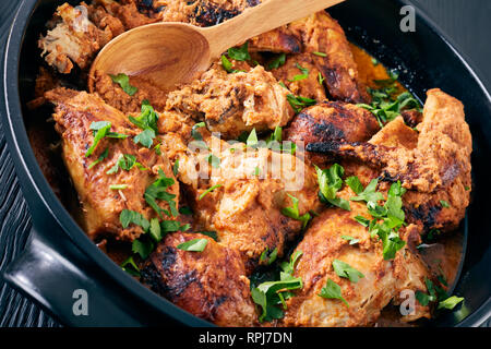 Kuku Paka, Kenyan chargrilled Chicken stewed in creamy spicy Coconut Sauce in a earthenware saucepan on a black wooden table, view from above, close-u Stock Photo