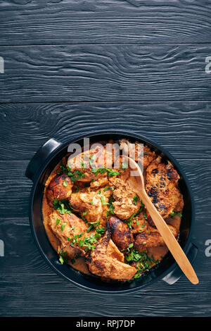 overhead view of Kuku Paka, Kenyan chargrilled Chicken in creamy spicy Coconut Sauce in a earthenware saucepan on a black wooden table, view from abov Stock Photo