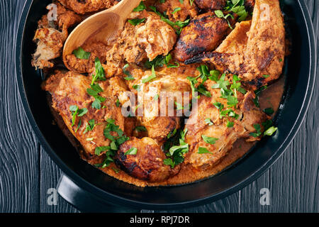 overhead view of Kuku Paka, Kenyan chargrilled Chicken in creamy spicy Coconut Sauce in a earthenware saucepan on a black wooden table, view from abov Stock Photo