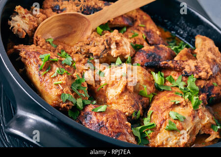 overhead view of Kuku Paka, Kenyan chargrilled Chicken in creamy spicy Coconut gravy in a earthenware saucepan on a black wooden table, view from abov Stock Photo