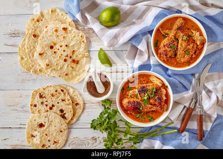 overhead view of Kuku Paka, Kenyan chargrilled Chicken in creamy spicy Coconut gravy served on a white bowls on an old wooden table with chapati, view Stock Photo