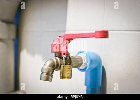 Tap with drinking water, the red valve is closed on the padlock. Water consumption concept Stock Photo