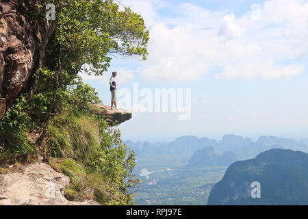 A man stands on a stone ledge in the mountains and overlooks the mountains below, Krabi, Thailand. Stock Photo