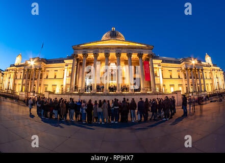London, England, UK - February 15, 2019: Group of tourists watching a show in front of National Gallery of Art and Culture in Trafalgar Square in even