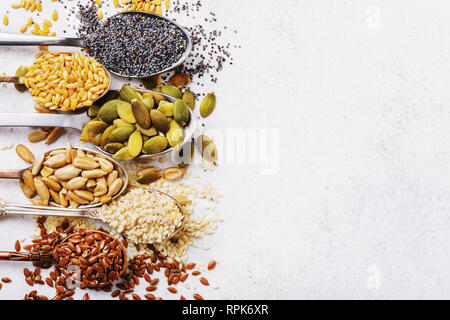 Seeds of pumpkin, flax, sesame, sunflower and poppy in metal spoons in the left part of a table with the copy of space, the top view Stock Photo