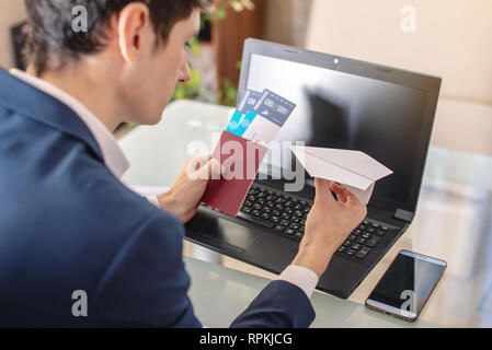 Businessman holding airline ticket and passport buying on the Internet using a laptop. Purchasing and booking airline tickets online Stock Photo