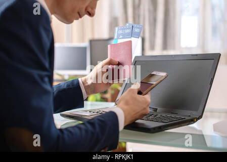 Man holding airline ticket and passport buying on the Internet using a laptop. Concept of purchasing and booking online Stock Photo