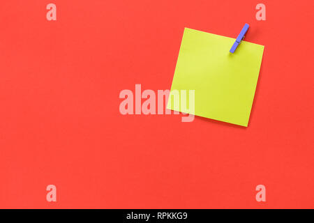 Yellow sticky note attached with a purple peg and copy space isolated on a red /orange background. Stock Photo