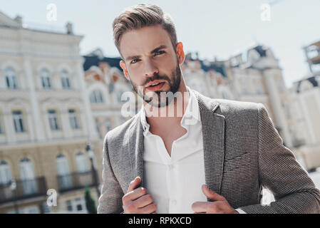Handsome young businessman walking on city street. He is going to work in office wear smart casual outfit of brown jacket and white shirt. Urban lifestyle of young professionals. Stock Photo