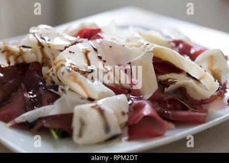 frontal closeup of a fresh spring proteic dish:a plate of bresaola with raspadura , soft and thin slaces and young parmesan cheese made in Lodi, north Stock Photo