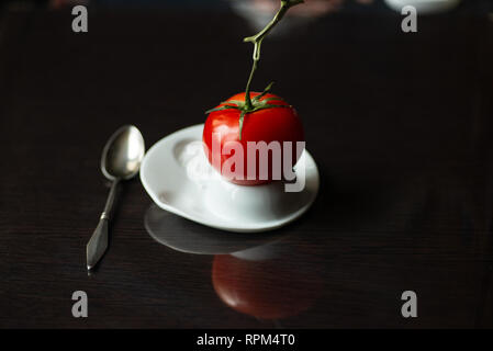 a bright red tomato on a branch hatched from an egg on dark background Stock Photo