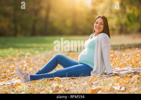 Happy pregnant woman relaxing in park. Stock Photo