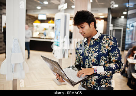 Young male indian freelancer sitting open laptop computer in fast food cafe, handsome asian man reading text message during work on net-book in comfor Stock Photo