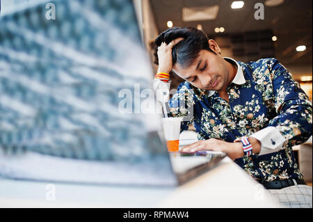 Young male indian freelancer sitting open laptop computer in fast food cafe, handsome exhausted asian during work on net-book in comfortable coffee sh Stock Photo