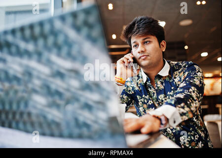 Young male indian freelancer sitting open laptop computer in fast food cafe, handsome asian man speaking phone during work on net-book in comfortable  Stock Photo