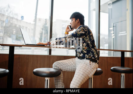 Young male indian freelancer sitting open laptop computer in fast food cafe, handsome asian man speaking phone during work on net-book in comfortable  Stock Photo