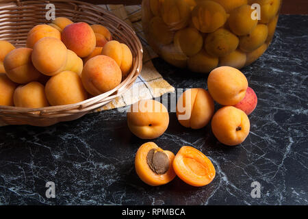 Ripe organic apricots harvested at summer time and big glass jar with canned sweet apricot compote on dark marble. Composition in rustic style - organ Stock Photo