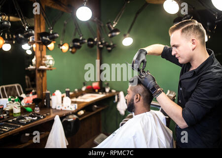 Handsome bearded man is smiling while having his hair cut by hairdresser at the barbershop Stock Photo