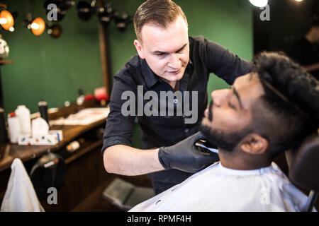 Close up Man with beard client in barbershop hairdresser Barber on shaving electric razor Stock Photo