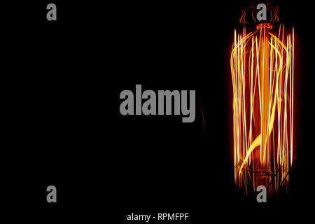 Close up of glowing filaments inside and Edison style bulb set against a dark background to the right of the frame. Stock Photo