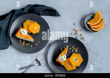 Dark plates with a slice of cake and oranges on a dark background, flat lay Stock Photo