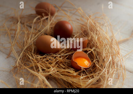 A group of eggs and one broken egg in hay on a wooden table Stock Photo