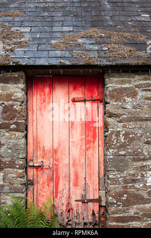 Red and distressed wooden door on an old stone barn with slate tile roof Stock Photo