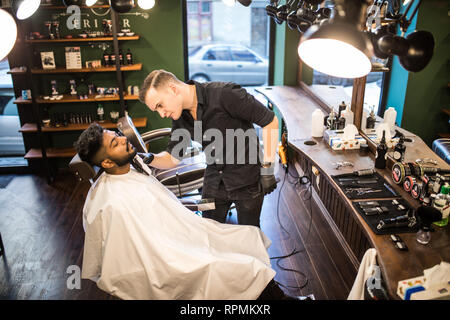 Close up Man with beard client in barbershop hairdresser Barber on shaving electric razor Stock Photo