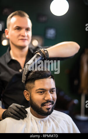 Finishing touch. Side view of hairdresser checking symmetry of haircut of his client at barbershop Stock Photo