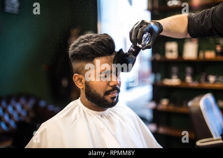 Barbers hand spread talcum powder on clients neck with professional shaving brush in barbershop salon.Male beauty treatment concept.Young black man ge