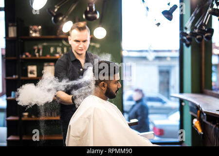 Bearded man with long beard, brutal, indian hipster with moustache, with stylish hair, haircut, getting powder on skin with make up brush by barber or Stock Photo