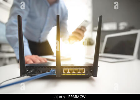 Wireless router with three antennas and cable connected. Man using smartphone in background Stock Photo